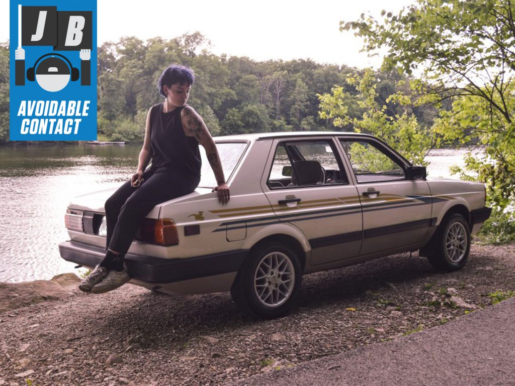 woman sits on car by riverbank
