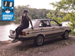woman sits on car by riverbank